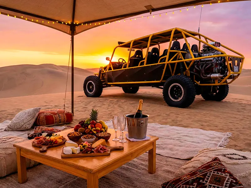 Montaje exclusivo de picnic de lujo con champagne y cena gourmet en las dunas del desierto de Paracas durante el atardecer.