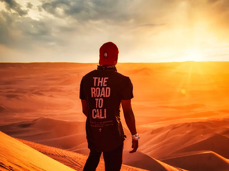 Turista deslizándose en tabla de Sandboarding desde la cima de una duna gigante en el desierto de Paracas.