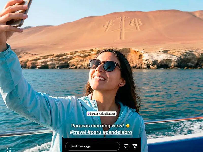 Turista feliz tomándose una selfie con el Candelabro de fondo desde el deslizador de Paracas Blue Tours.