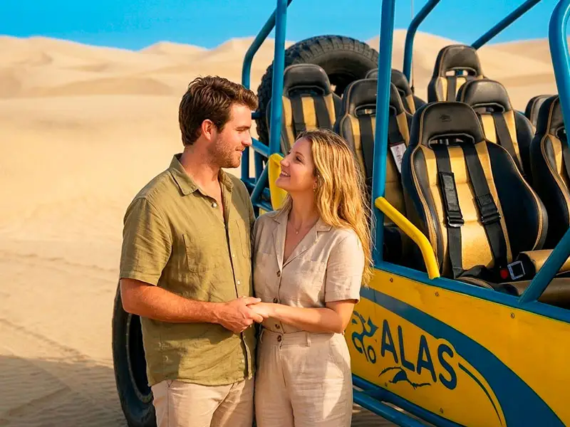 Pareja elegante abrazándose junto a un tubular de alta ingeniería en la cima de una duna virgen en Paracas