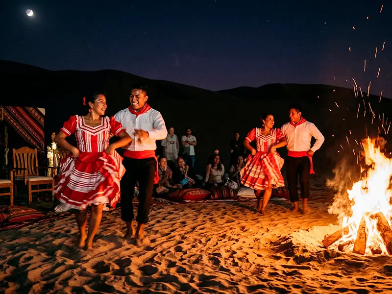 Bailarines de festejo afroperuano realizando un show con energía cerca de una fogata en el desierto de California.