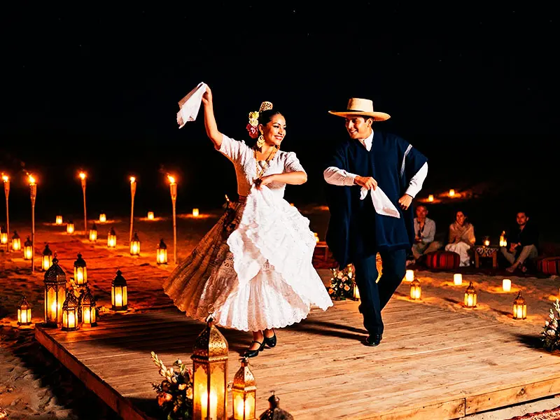 Pareja de bailarines de Marinera Norteña realizando una coreografía de gala en el desierto de Paracas iluminado por antorchas.